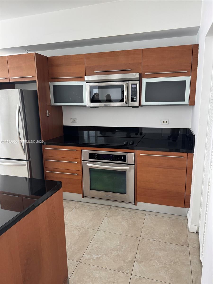 A kitchen features wood cabinets, stainless steel appliances, and black countertops — 253 NE 2nd St # 1108, Miami FL 33132, MIAMI, FL
