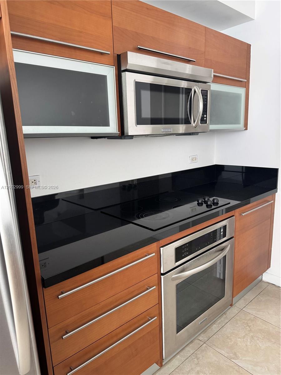 A kitchen features wood cabinets, stainless steel appliances, and a black countertop — 253 NE 2nd St # 1108, Miami FL 33132, MIAMI, FL