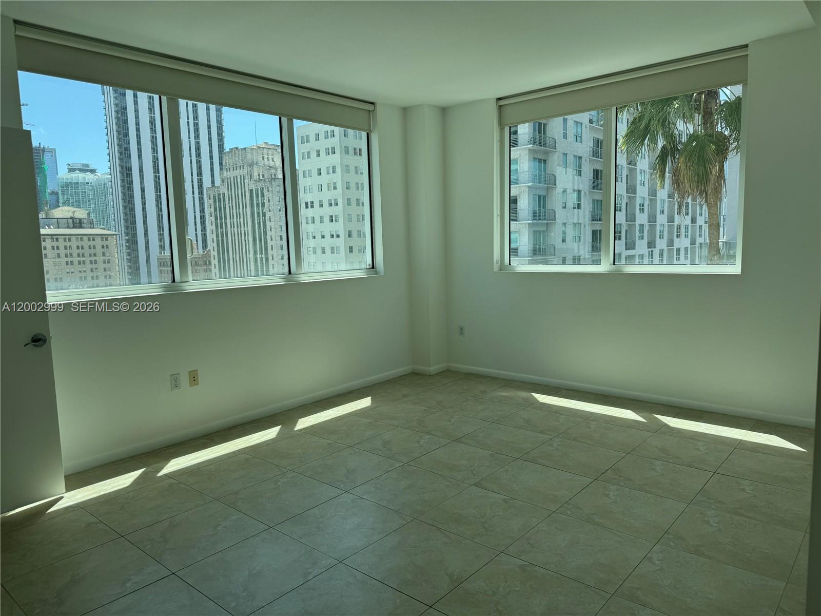 An empty room with light-colored tile flooring and large windows overlooking city buildings — 253 NE 2nd St # 1108, Miami FL 33132, MIAMI, FL