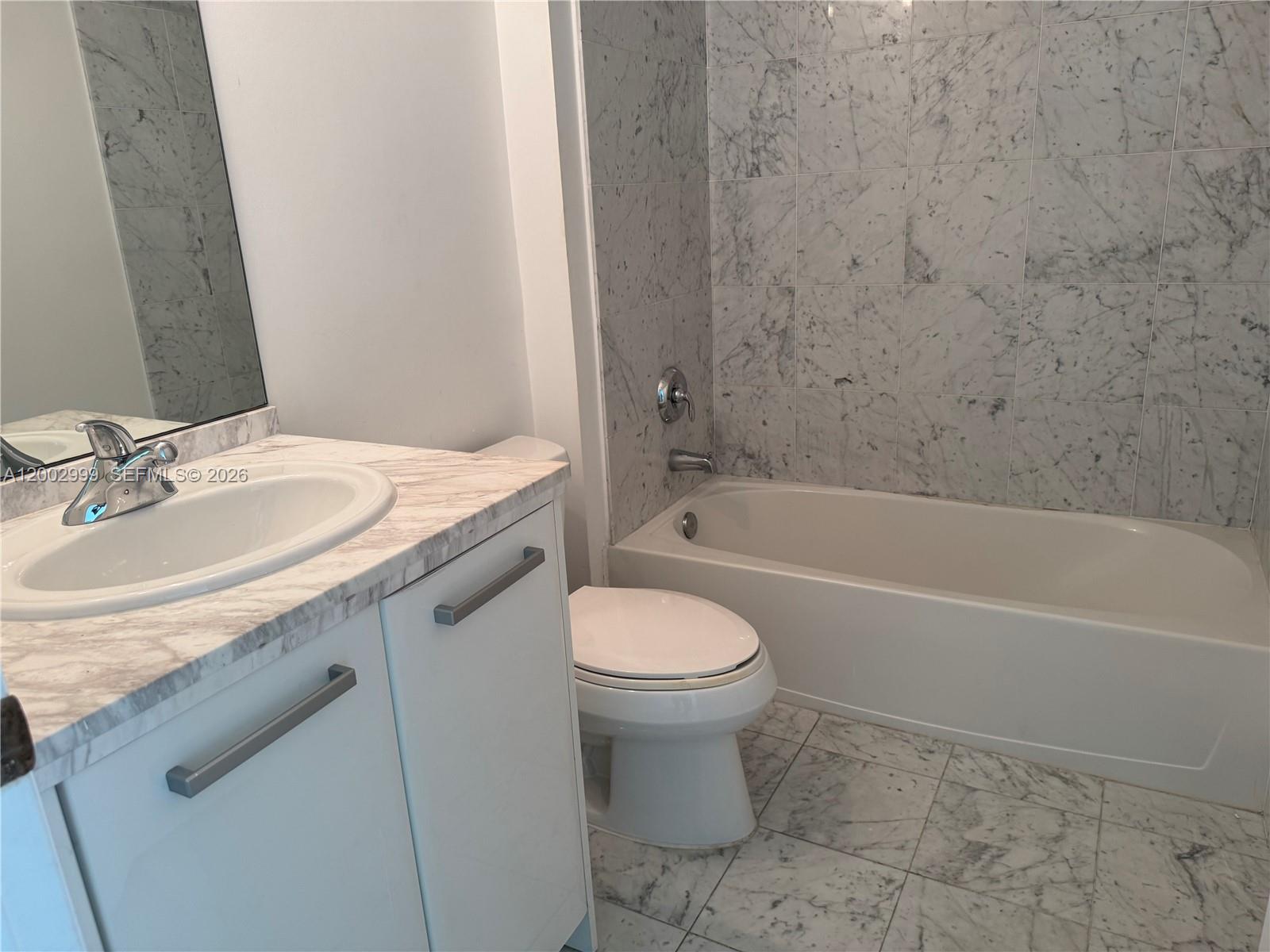 A bathroom features a marble-topped vanity, a white toilet, and a marble-tiled bathtub surround — 253 NE 2nd St # 1108, Miami FL 33132, MIAMI, FL