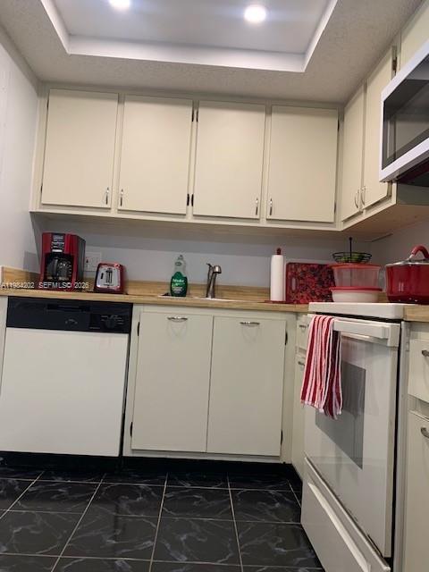 A kitchen features white cabinets, a black dishwasher, a white stove, and black tiled flooring — 5530 NW 44th St # 111C, Lauderhill FL 33319, LAUDERHILL, FL
