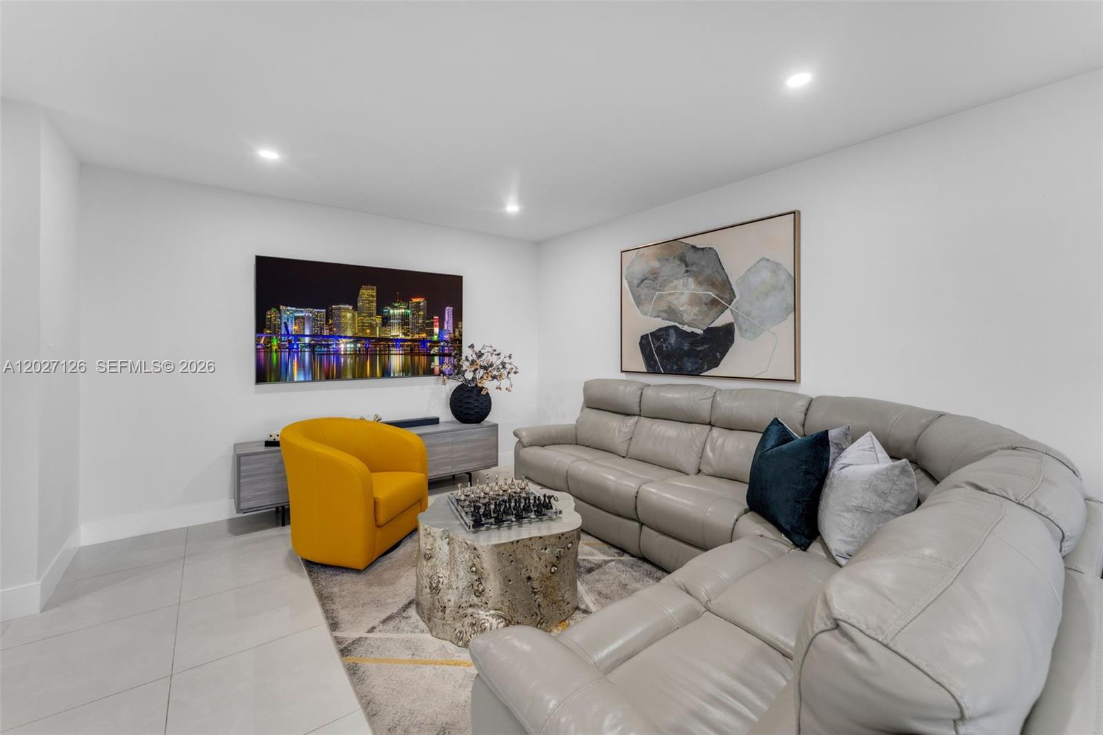 A living room features a grey sectional sofa, a yellow armchair, and a city-themed television — 1350 SW 122nd Ave # 415, Miami FL 33184, MIAMI, FL