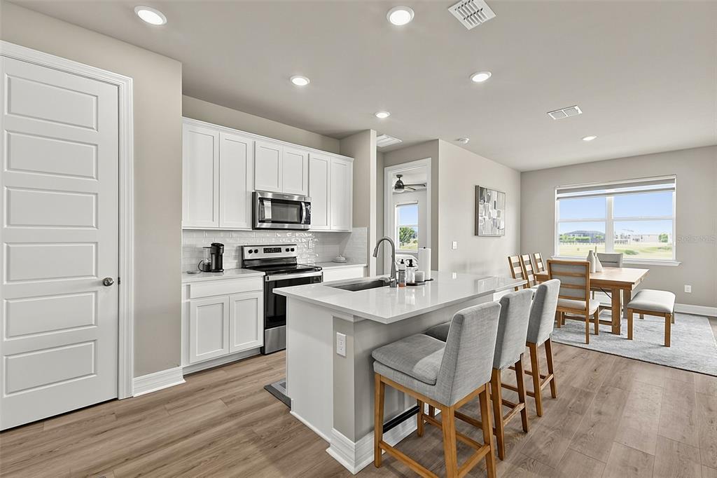 A modern kitchen features white cabinetry, a quartz island with bar seating, and wood flooring — 44317 TIMBERLAND TERRACE, PUNTA GORDA, FL