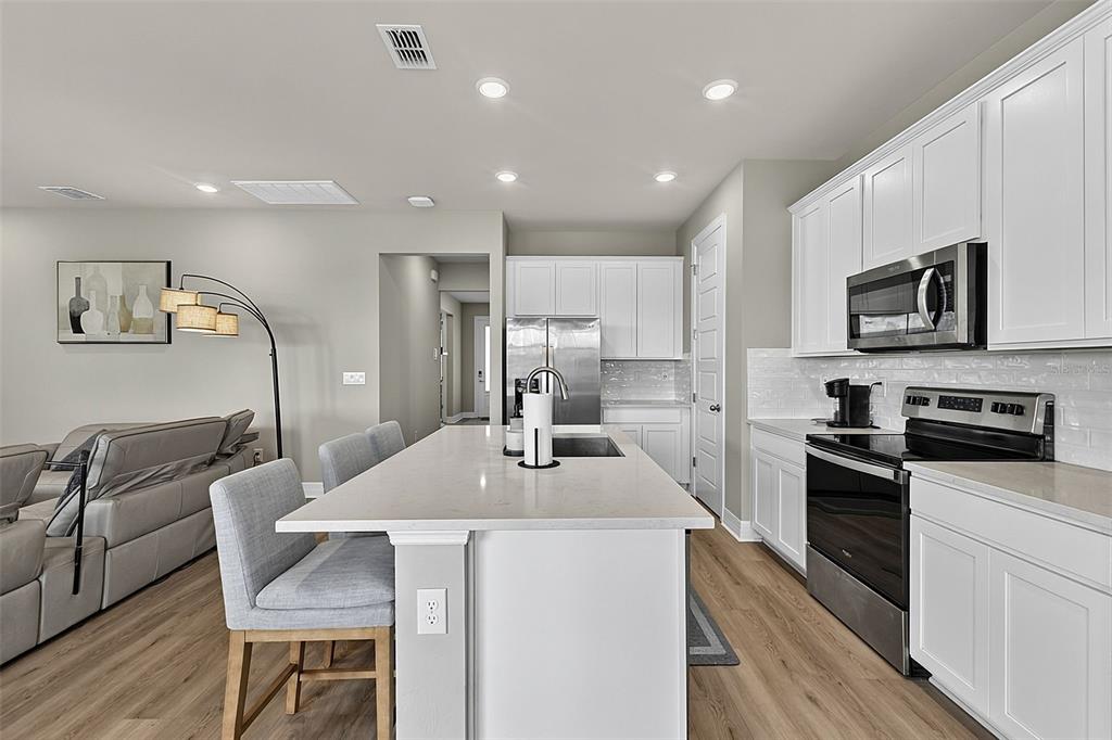 A modern kitchen features white cabinetry, a central island with bar seating, and stainless appliances — 44317 TIMBERLAND TERRACE, PUNTA GORDA, FL