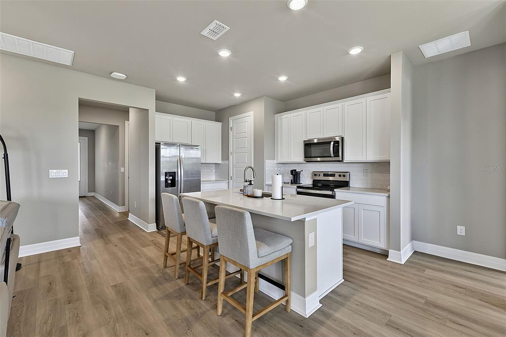 A modern kitchen features white cabinets, stainless steel appliances, and a central island with seating — 44317 TIMBERLAND TERRACE, PUNTA GORDA, FL