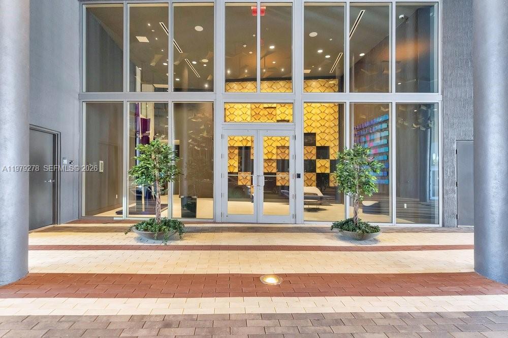 The exterior entrance features glass double doors flanked by two potted trees on a paved walkway — 3900 Biscayne Blvd # 1101, Miami FL 33137, MIAMI, FL