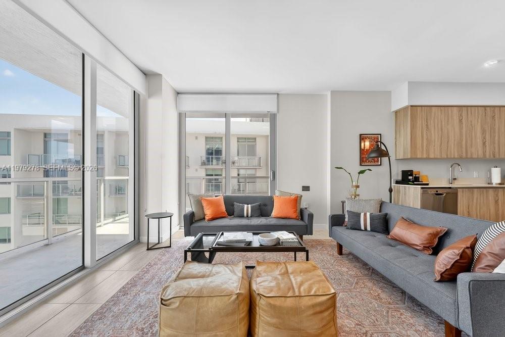 A modern living room features two gray sofas, leather ottomans, and large floor-to-ceiling windows — 3900 Biscayne Blvd # 1101, Miami FL 33137, MIAMI, FL