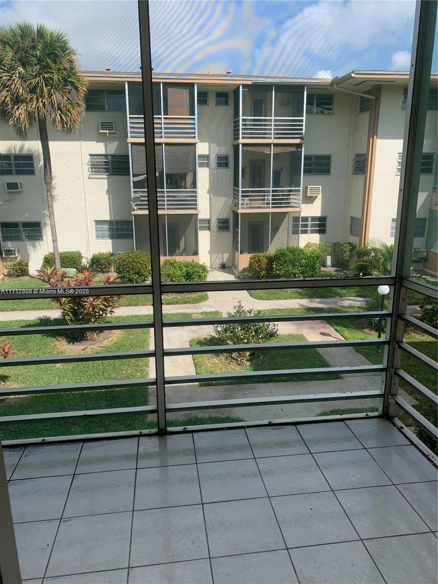 A tiled balcony with a metal screen enclosure overlooks a courtyard and apartment building — 1395 NE 167th St # 209, Miami FL 33162, MIAMI, FL