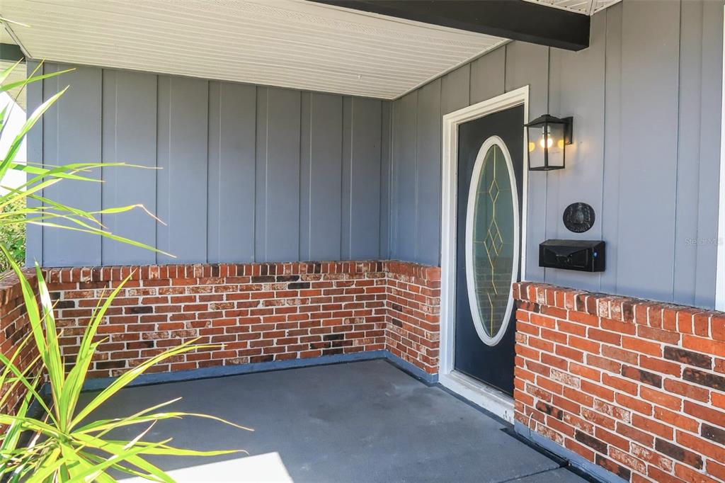 A covered porch features a gray front door with an oval glass insert and brick — 806 OAKMONT AVENUE, SUN CITY CENTER, FL