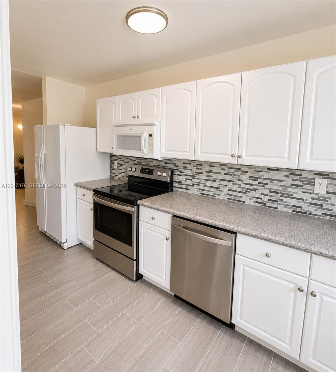 A kitchen features white cabinets, stainless steel appliances, granite countertops, and a gray tile backsplash — 270 E Layne Blvd # 110, Hallandale Beach FL 33009, HALLANDALE BEACH, FL