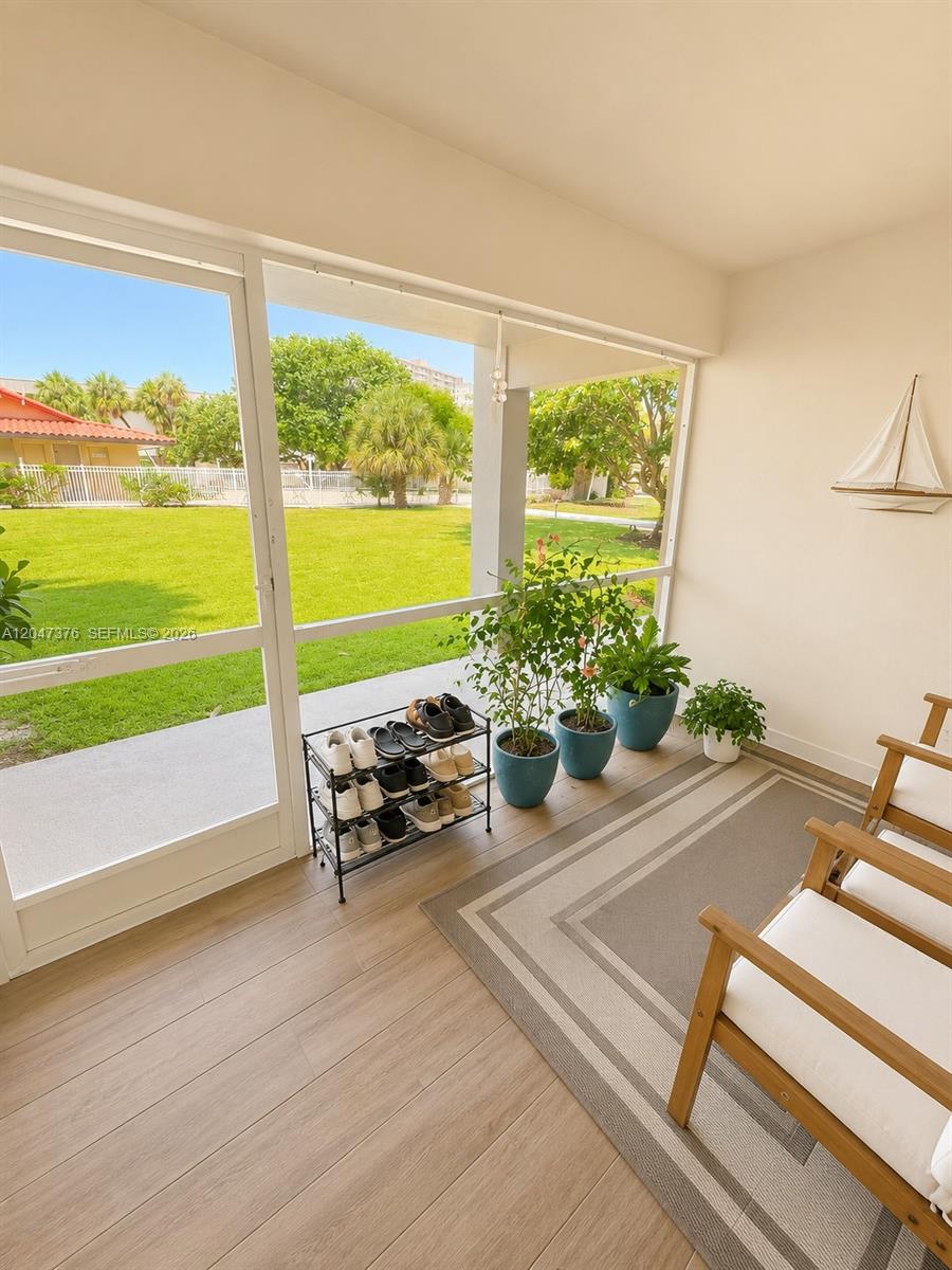 A screened-in patio features light wood-look flooring, a shoe rack, potted plants, and outdoor views — 270 E Layne Blvd # 110, Hallandale Beach FL 33009, HALLANDALE BEACH, FL