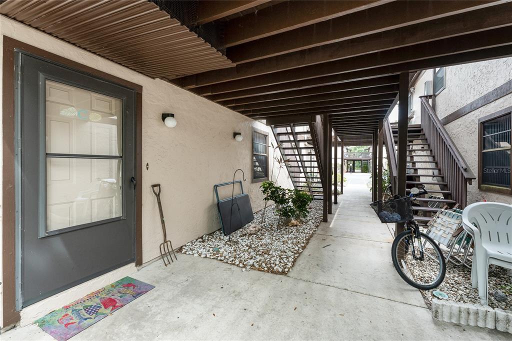 A covered ground-level patio features a concrete floor, a gravel garden bed, and wooden stairs — 4022 BEAVER LANE UNIT 500C, PORT CHARLOTTE, FL