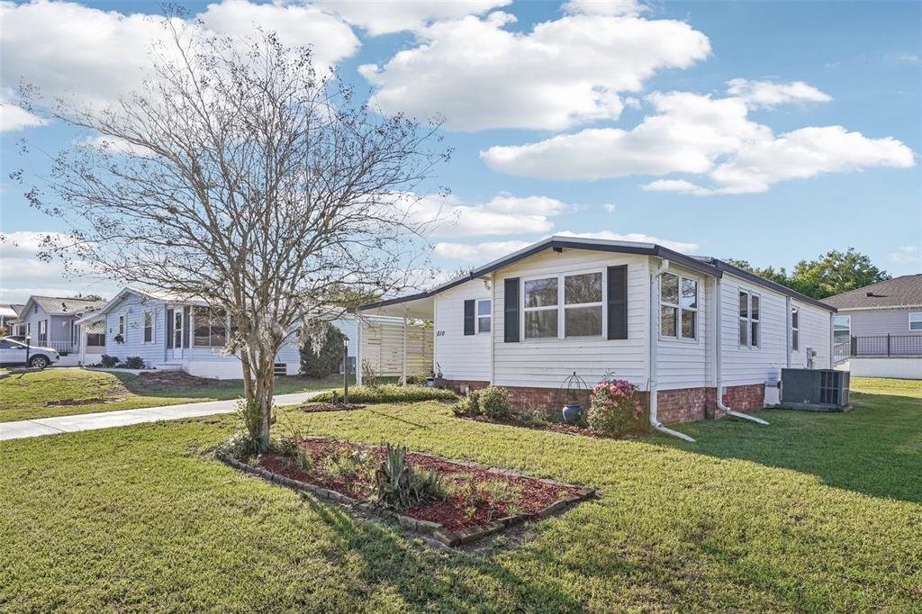 A white single-story manufactured home with a brick base and a front yard tree — 510 BONITA DRIVE, LADY LAKE, FL