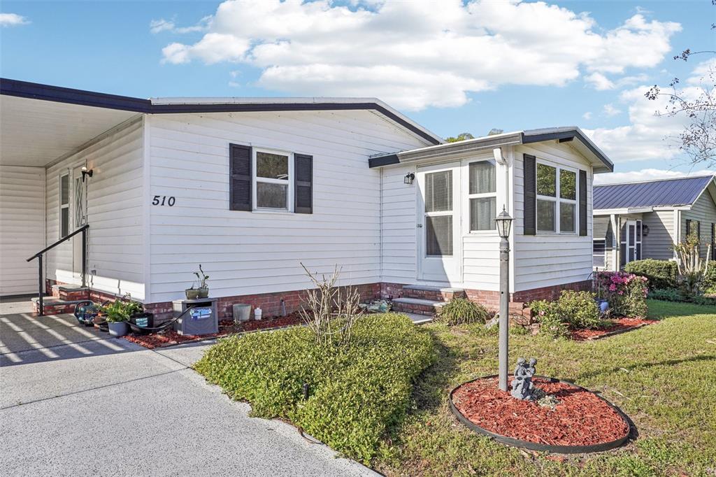 A white mobile home with a brick base, a carport, and a small front yard — 510 BONITA DRIVE, LADY LAKE, FL