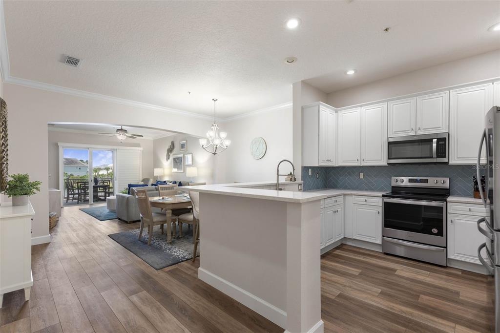 A kitchen with white cabinets and a blue backsplash opens to a dining area — 1100 CINNAMON BEACH WAY UNIT 1024, PALM COAST, FL