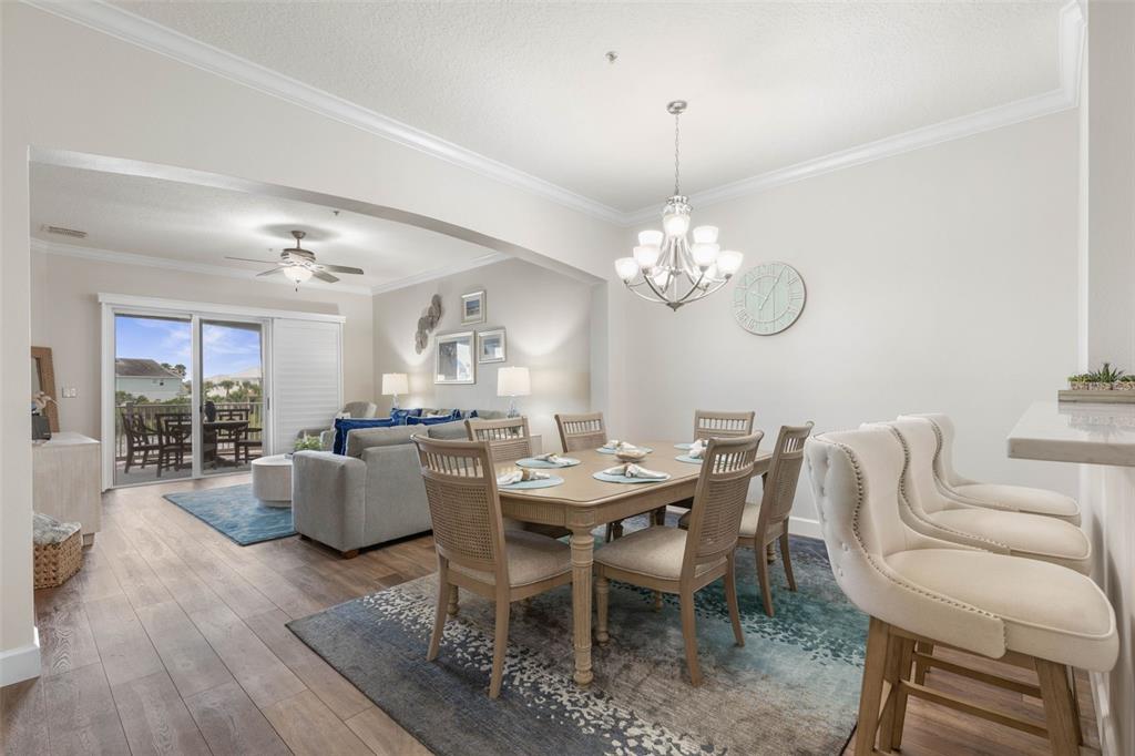 A dining area with a chandelier and table flows into a living room with balcony access — 1100 CINNAMON BEACH WAY UNIT 1024, PALM COAST, FL