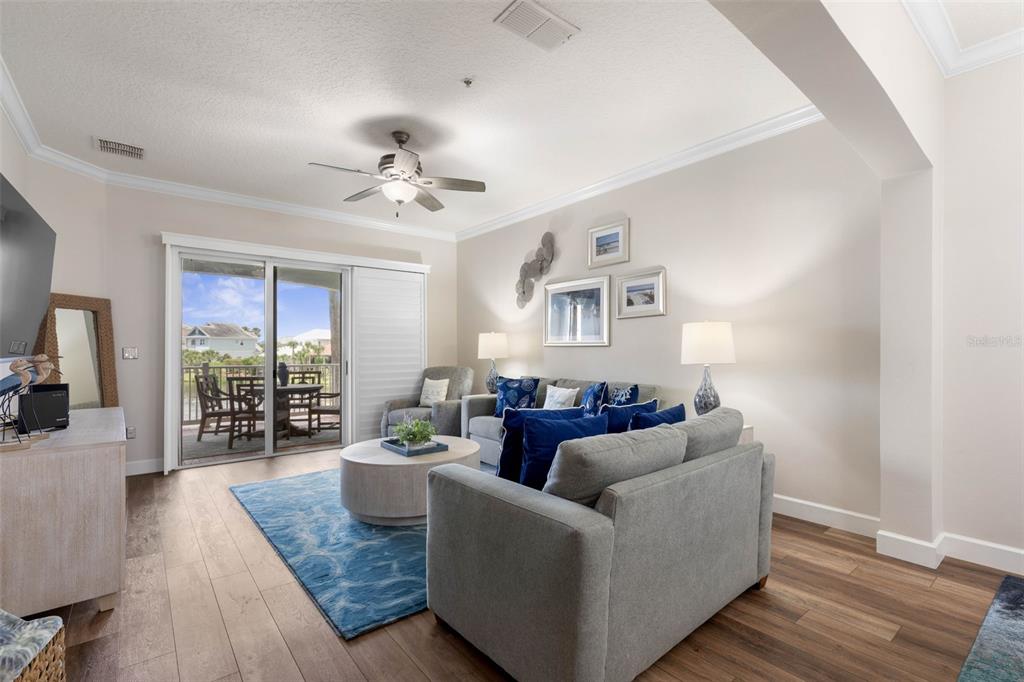 A living room with a gray sofa, blue rug, and sliding doors leading to a balcony — 1100 CINNAMON BEACH WAY UNIT 1024, PALM COAST, FL