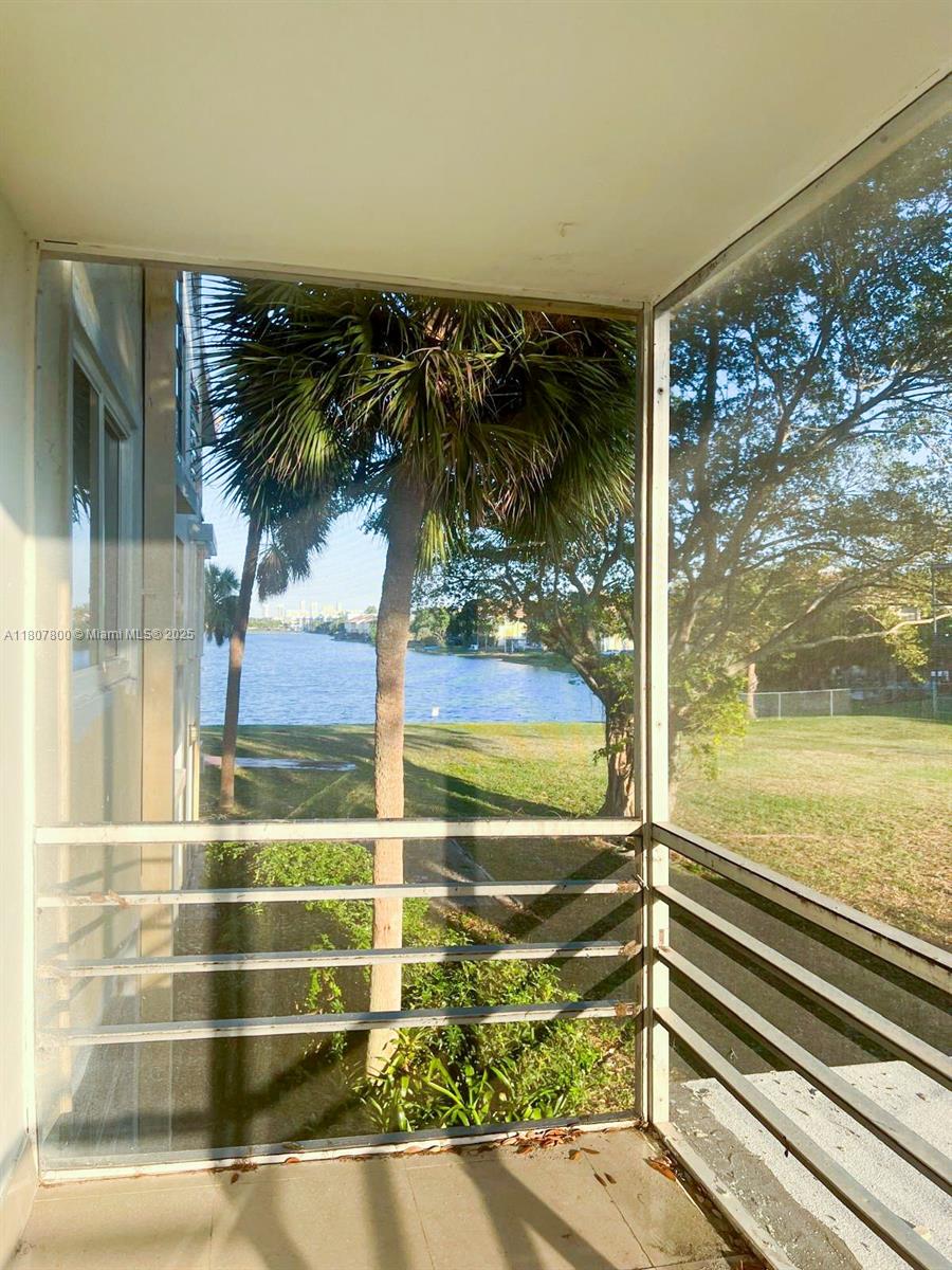 A screened-in balcony overlooks a grassy lawn and a lake with palm trees — 447 NE 195th St # 217, Miami FL 33179, MIAMI, FL