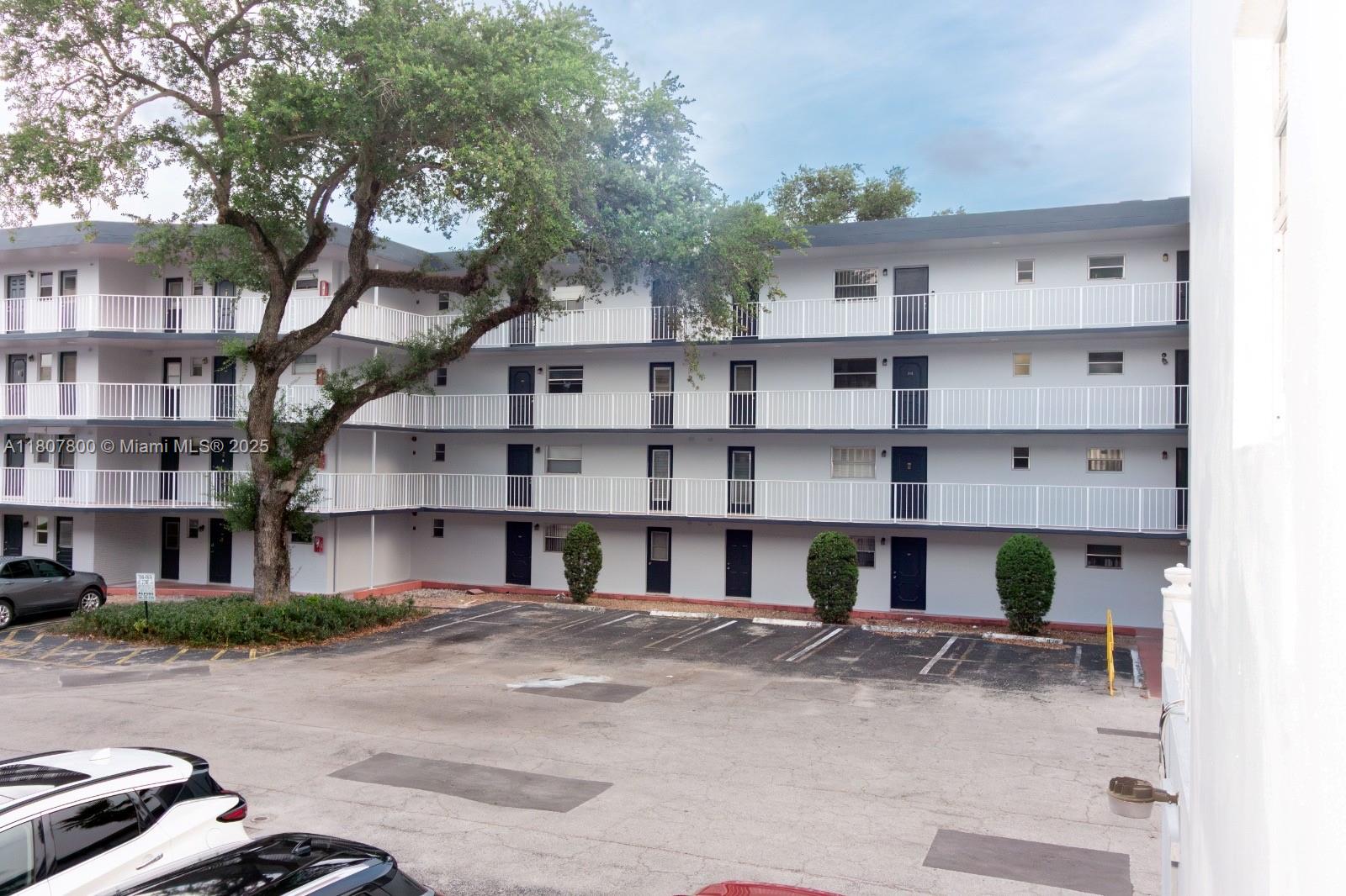 A multi-story apartment building features exterior walkways, dark doors, and a paved parking lot — 447 NE 195th St # 217, Miami FL 33179, MIAMI, FL