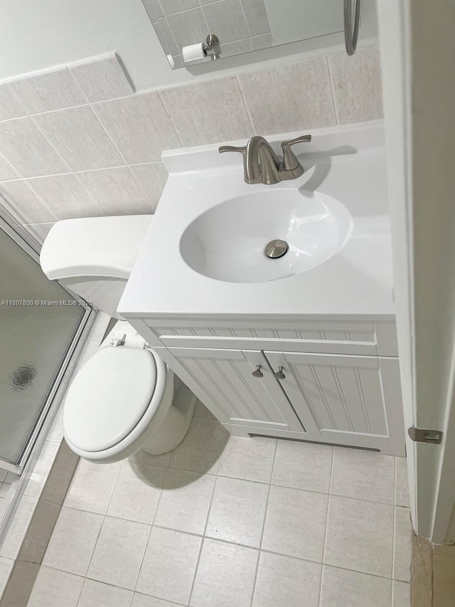 A bathroom features a white vanity with a sink, a toilet, and tiled walls — 447 NE 195th St # 217, Miami FL 33179, MIAMI, FL