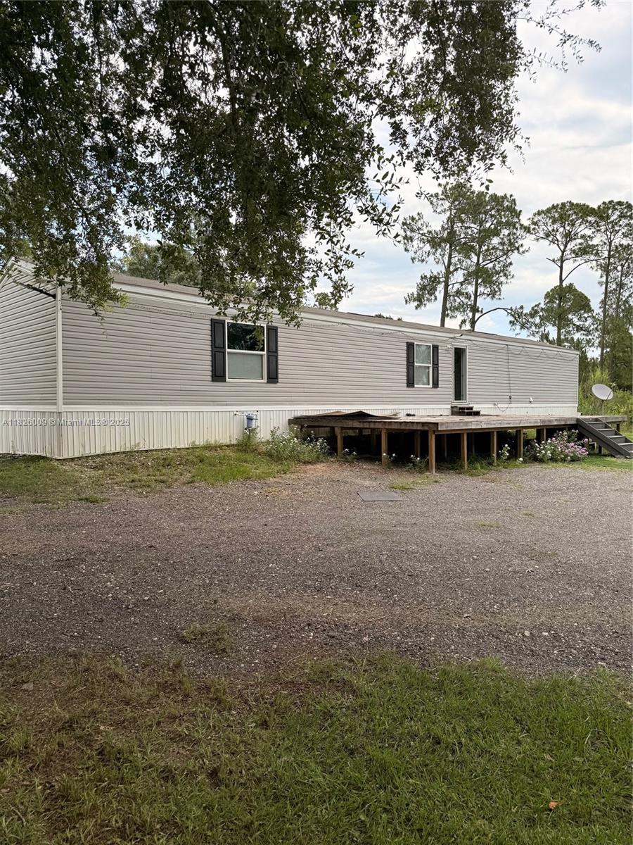 A single-story manufactured home with light gray siding and a wooden deck sits on gravel — 751 appaloosa Ave, Clewiston FL 33440, CLEWISTON, FL