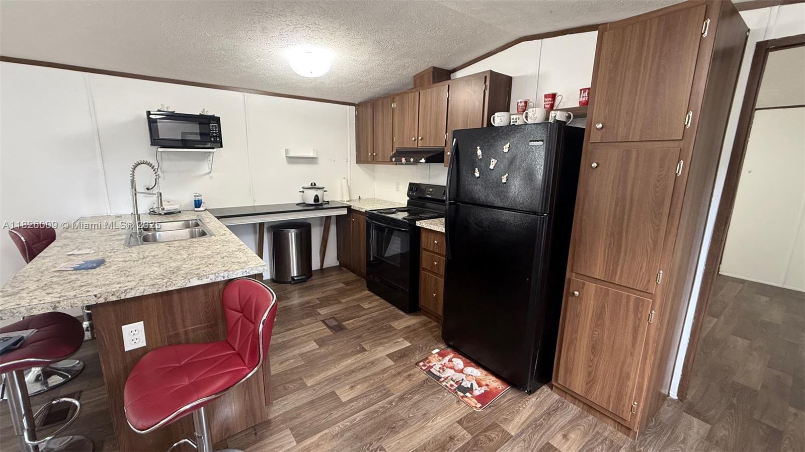 A kitchen features wood-look flooring, dark wood cabinetry, black appliances, and a granite-topped island — 751 appaloosa Ave, Clewiston FL 33440, CLEWISTON, FL