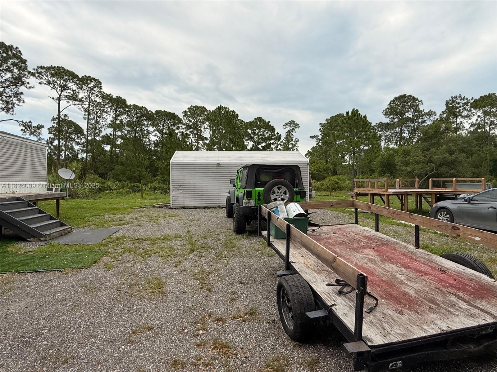 A green Jeep is hitched to a flatbed trailer parked on a gravel lot — 751 appaloosa Ave, Clewiston FL 33440, CLEWISTON, FL