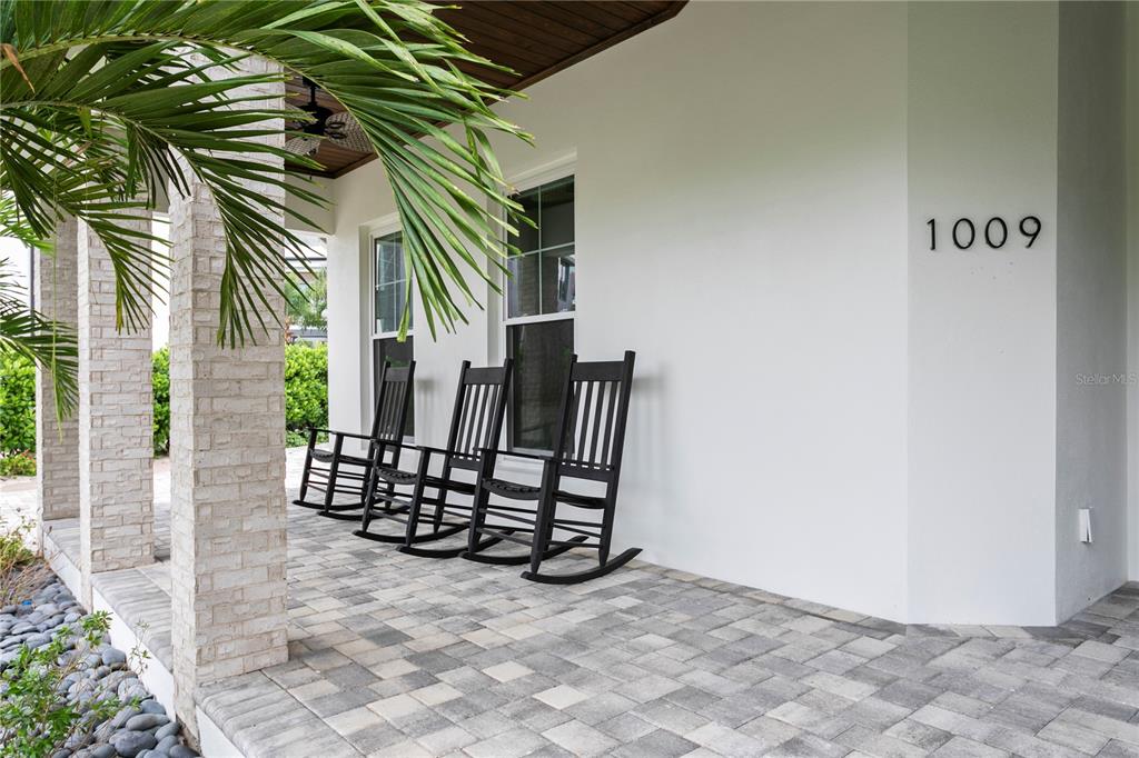 A covered front porch features light-colored brick columns, a paver floor, and three black rocking chairs — 1009 S MORRISON COURT, TAMPA, FL