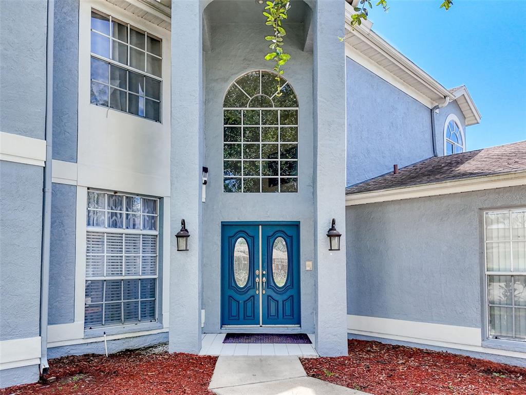 A two-story house exterior features a blue facade, double front doors, and a large window — 13002 SAINT FILAGREE DRIVE, RIVERVIEW, FL