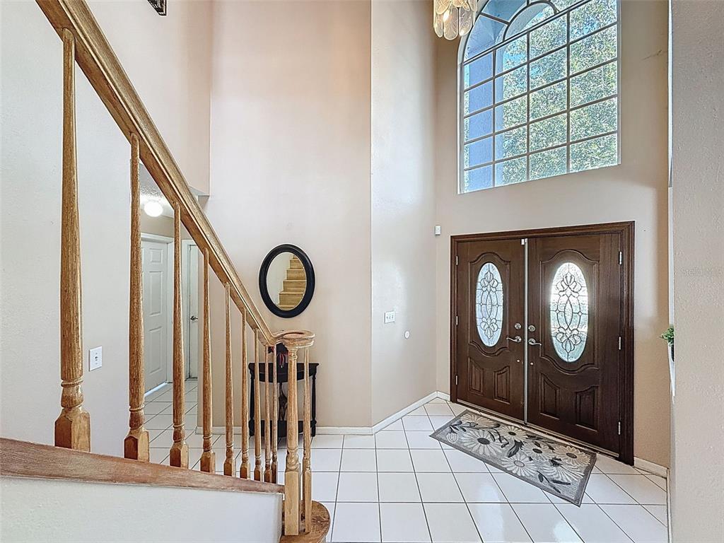 A two-story foyer features white tile flooring, a wooden staircase, and a large arched window — 13002 SAINT FILAGREE DRIVE, RIVERVIEW, FL