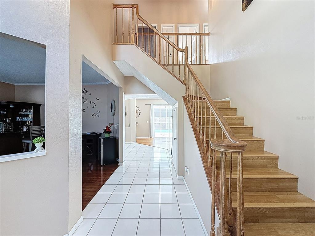 A foyer features a wooden staircase, white tile flooring, and an opening to a living area — 13002 SAINT FILAGREE DRIVE, RIVERVIEW, FL