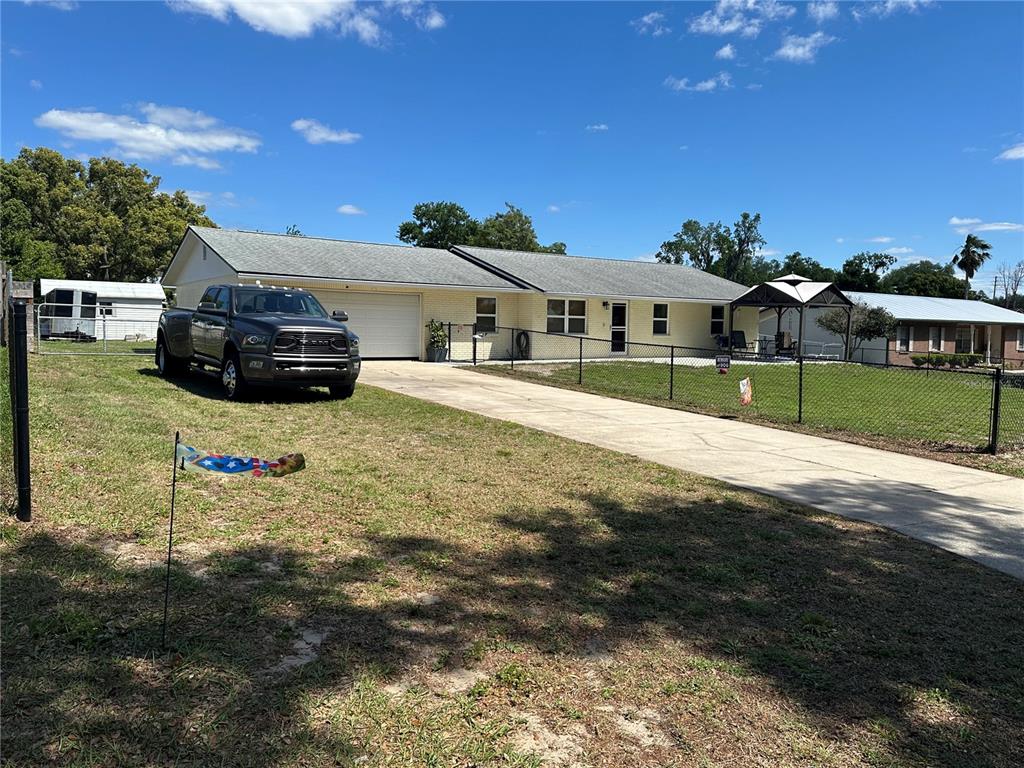 A single-story house with a light-colored exterior, a concrete driveway, and a chain-link fence — 7411 ORANGE CREST CIRCLE, LAKELAND, FL