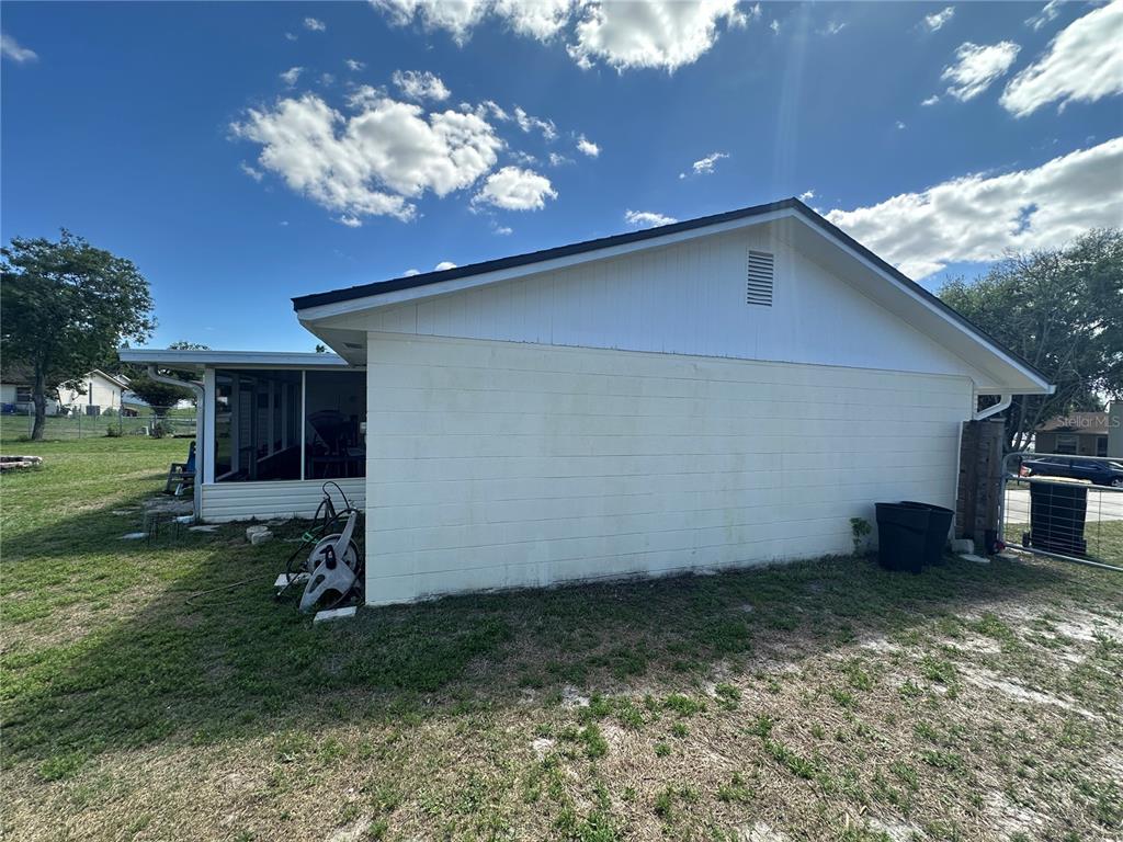 The exterior side of a house features a concrete block wall and a screened-in porch — 7411 ORANGE CREST CIRCLE, LAKELAND, FL