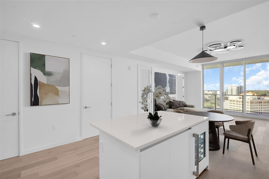 A modern kitchen island with a white countertop sits before a dining area and balcony — 400 CENTRAL AVENUE UNIT 1009, ST PETERSBURG, FL