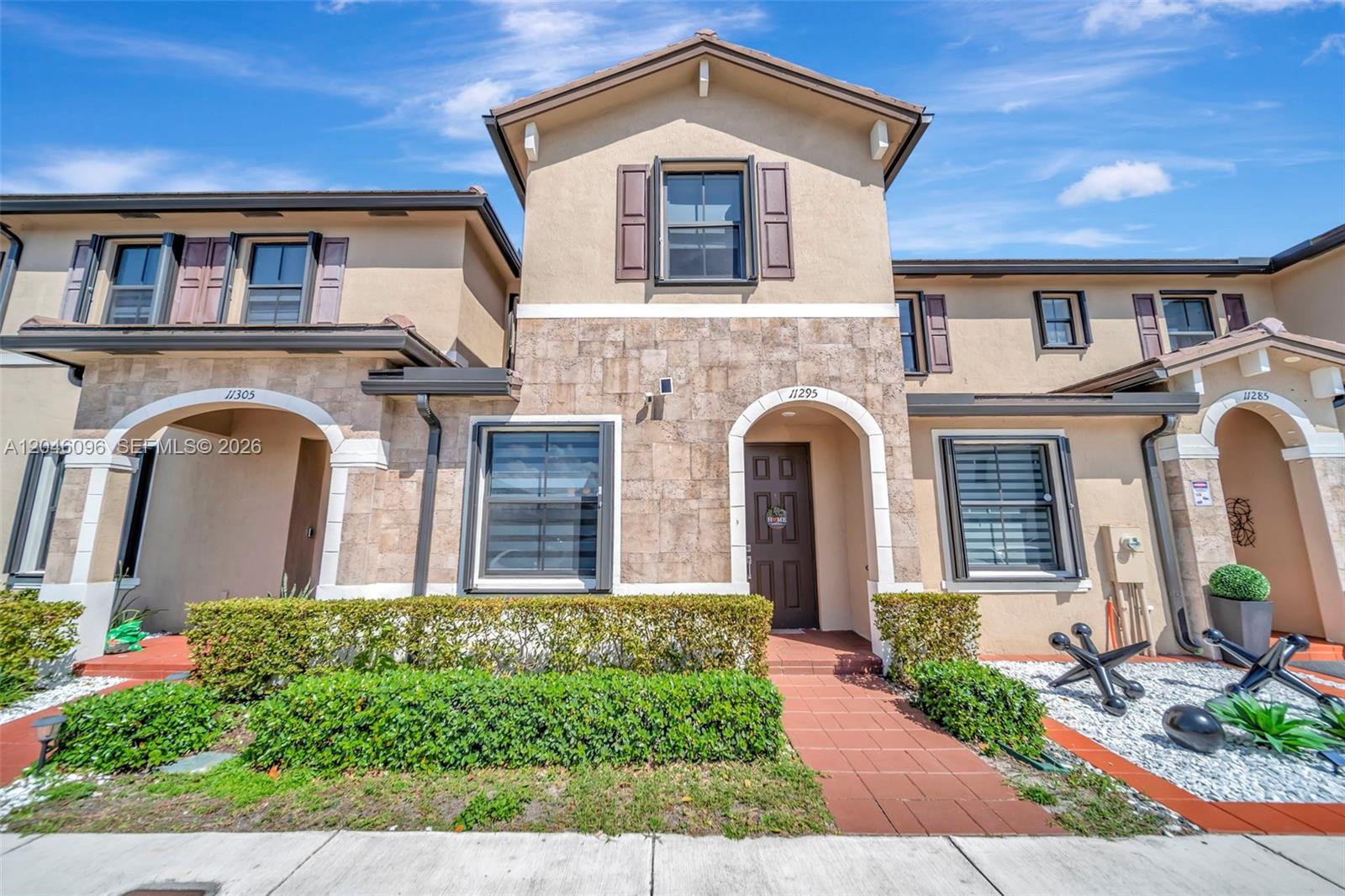 A two-story townhouse exterior features a stone facade, arched entryways, and a manicured hedge — 11295 W 34th Way, Hialeah FL 33018, HIALEAH, FL