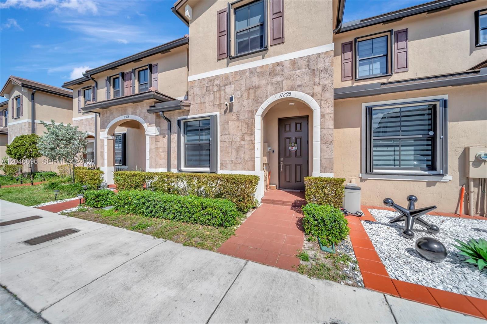 A two-story townhouse exterior features tan stucco, stone accents, brown shutters, and a front walkway — 11295 W 34th Way, Hialeah FL 33018, HIALEAH, FL