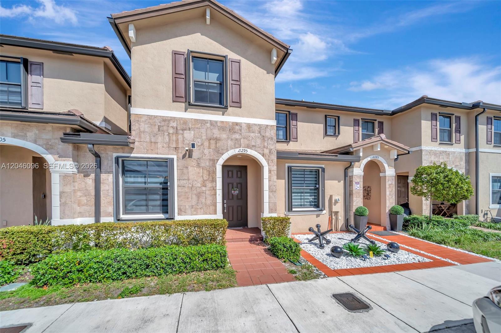 A two-story townhouse exterior features tan stucco, stone veneer, brown shutters, and a tiled walkway — 11295 W 34th Way, Hialeah FL 33018, HIALEAH, FL