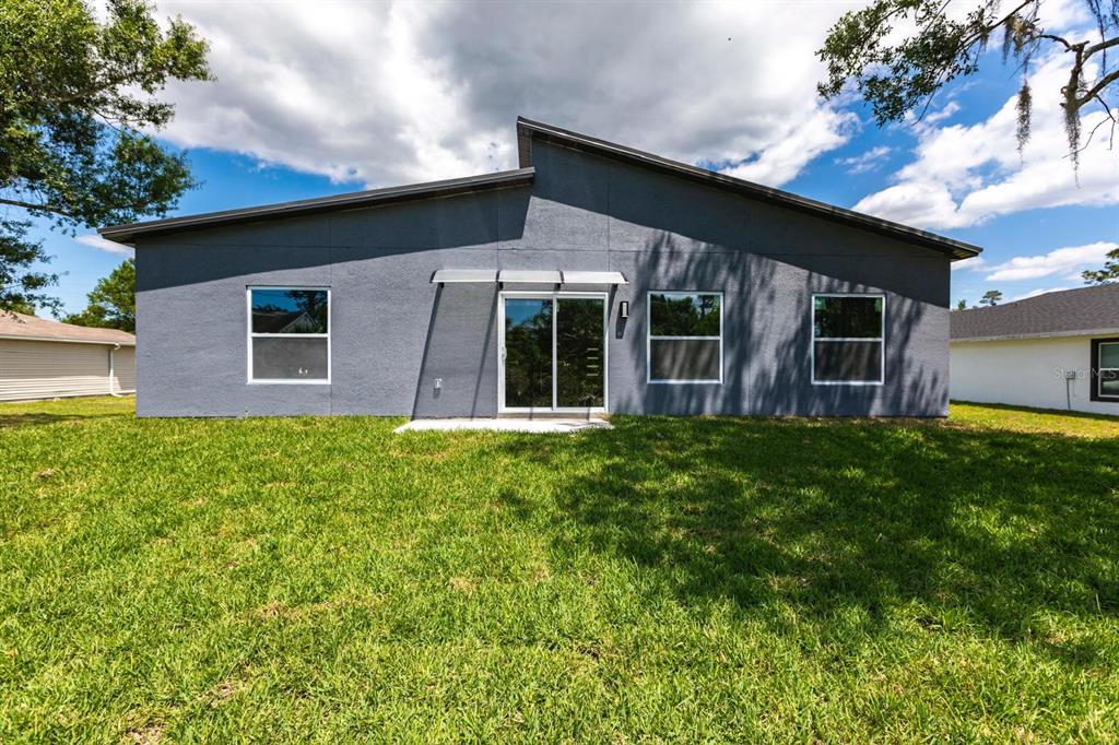 The rear exterior of a gray single-story house features a sliding glass door and windows — 958 GABLE STREET, LEHIGH ACRES, FL