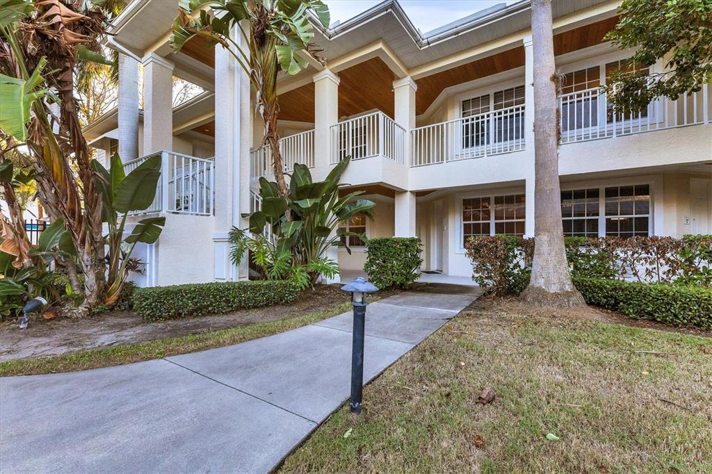 A two-story building exterior features white stucco walls, a covered walkway, and tropical landscaping — 3506 54TH DRIVE W UNIT 104, BRADENTON, FL
