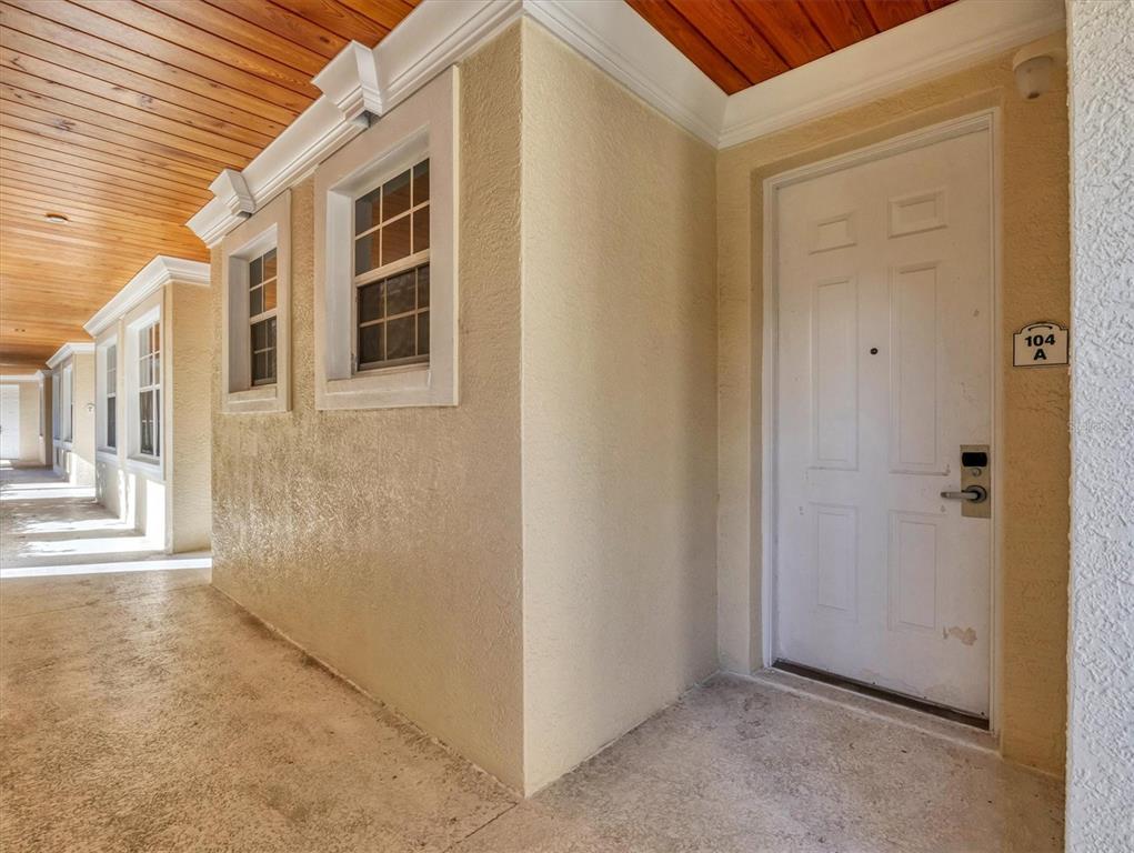 A white front door labeled 104A sits on a covered walkway with wood-paneled ceilings — 3506 54TH DRIVE W UNIT 104, BRADENTON, FL