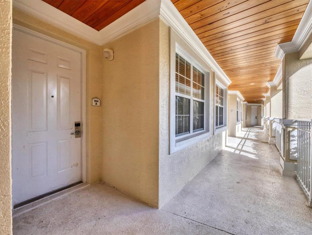 A white door with a keypad lock sits on a covered outdoor walkway with wood-paneled ceilings — 3506 54TH DRIVE W UNIT 104, BRADENTON, FL