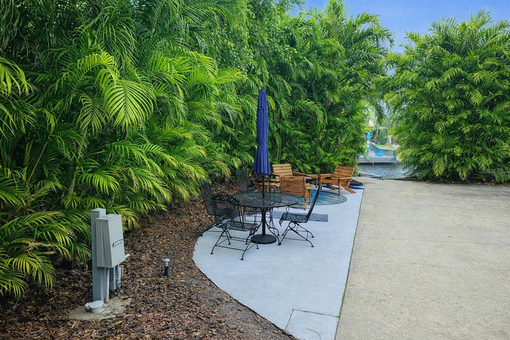 A patio with a dining set and lounge chairs sits beside a canal and lush foliage — 443 WATERWAY DRIVE, LAKE WALES, FL