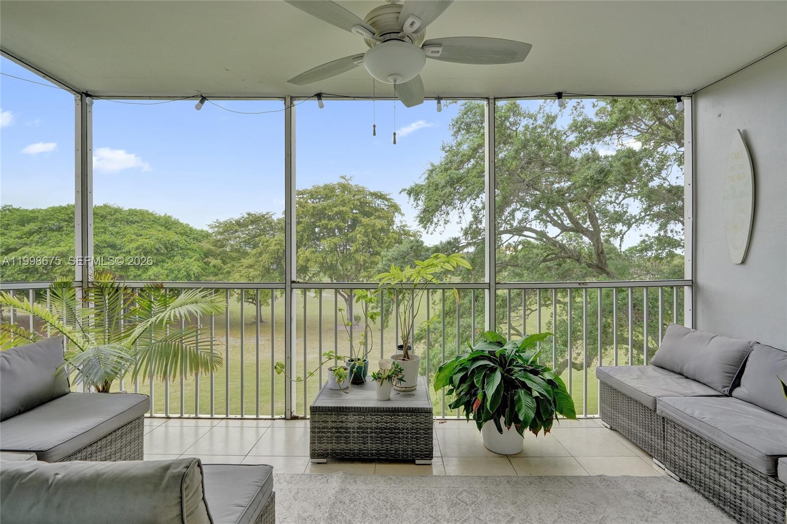 A screened-in balcony features gray wicker furniture, potted plants, and a view of trees — 2651 S Course Dr # 410, Pompano Beach FL 33069, POMPANO BEACH, FL