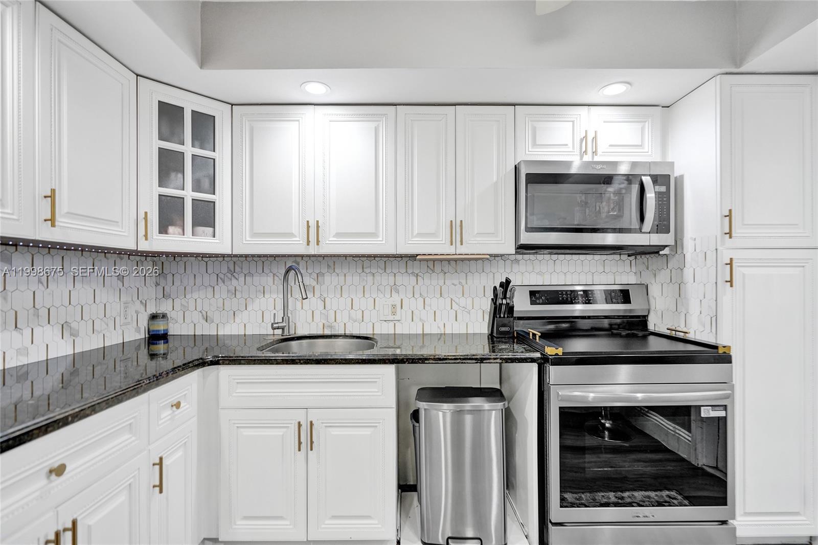 A kitchen features white cabinets, stainless steel appliances, a dark countertop, and a hexagonal backsplash — 2651 S Course Dr # 410, Pompano Beach FL 33069, POMPANO BEACH, FL