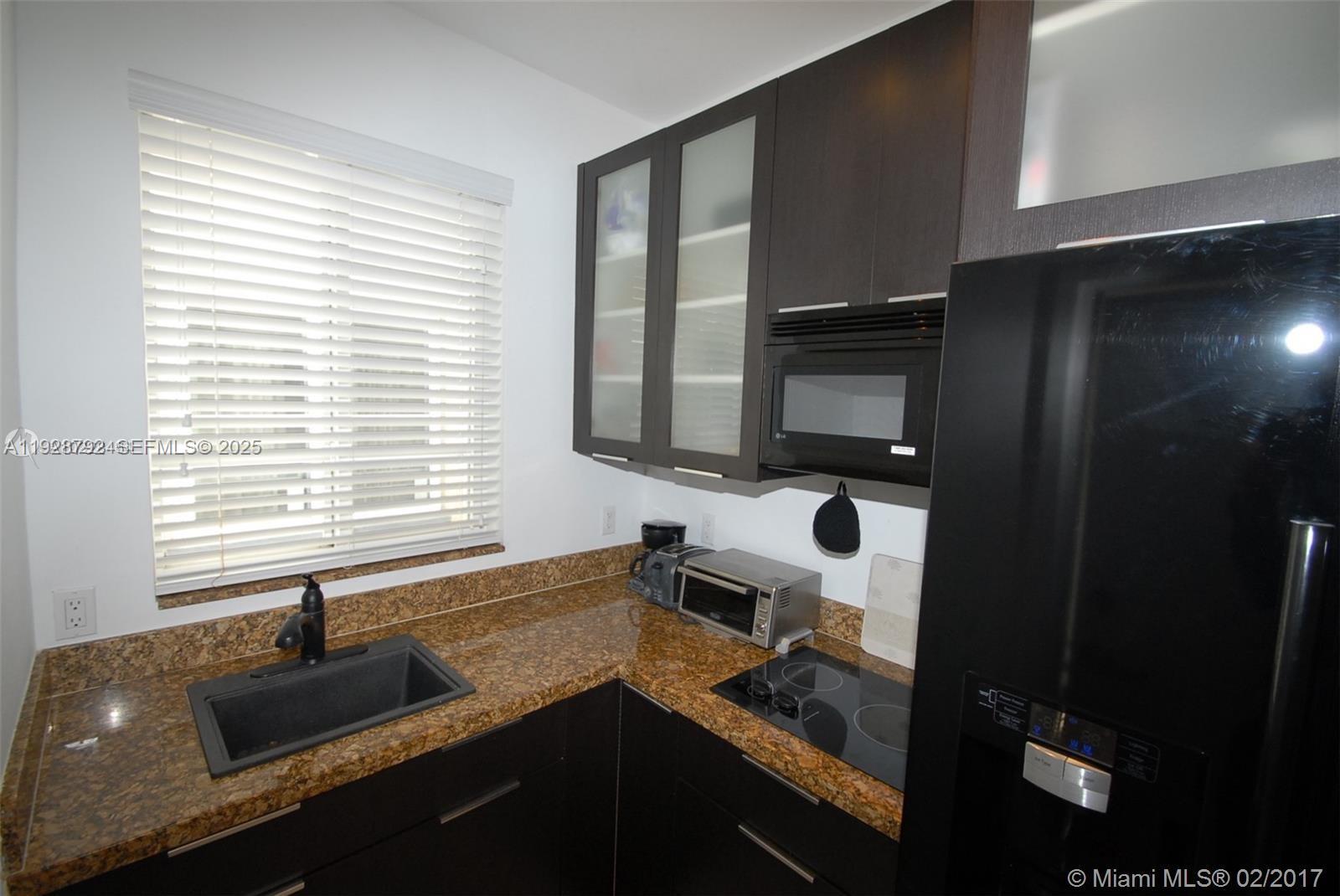 A kitchen features dark cabinets, granite countertops, a black sink, and a black refrigerator — 1000 Meridian Ave # 23, Miami Beach FL 33139, MIAMI BEACH, FL