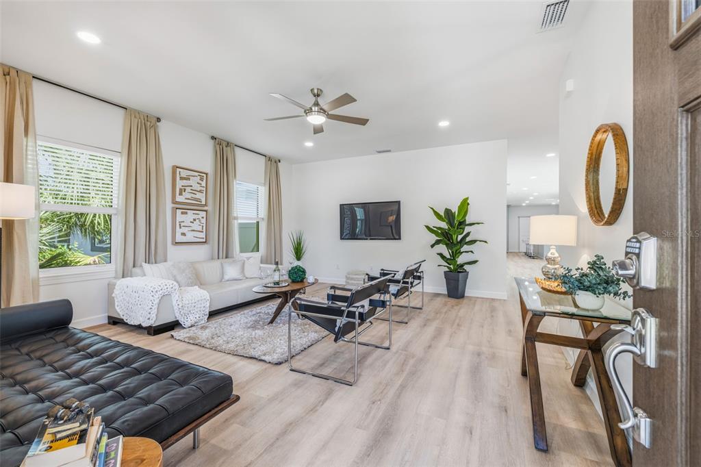 A bright living room features light wood flooring, a white sofa, and modern black chairs — 494 39TH AVENUE N, ST PETERSBURG, FL
