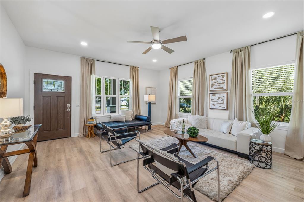 A living room features light wood flooring, a white sofa, two black chairs, and windows — 494 39TH AVENUE N, ST PETERSBURG, FL