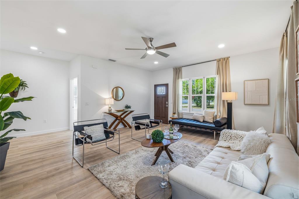 A bright living room features light wood flooring, a white sofa, and two modern armchairs — 494 39TH AVENUE N, ST PETERSBURG, FL
