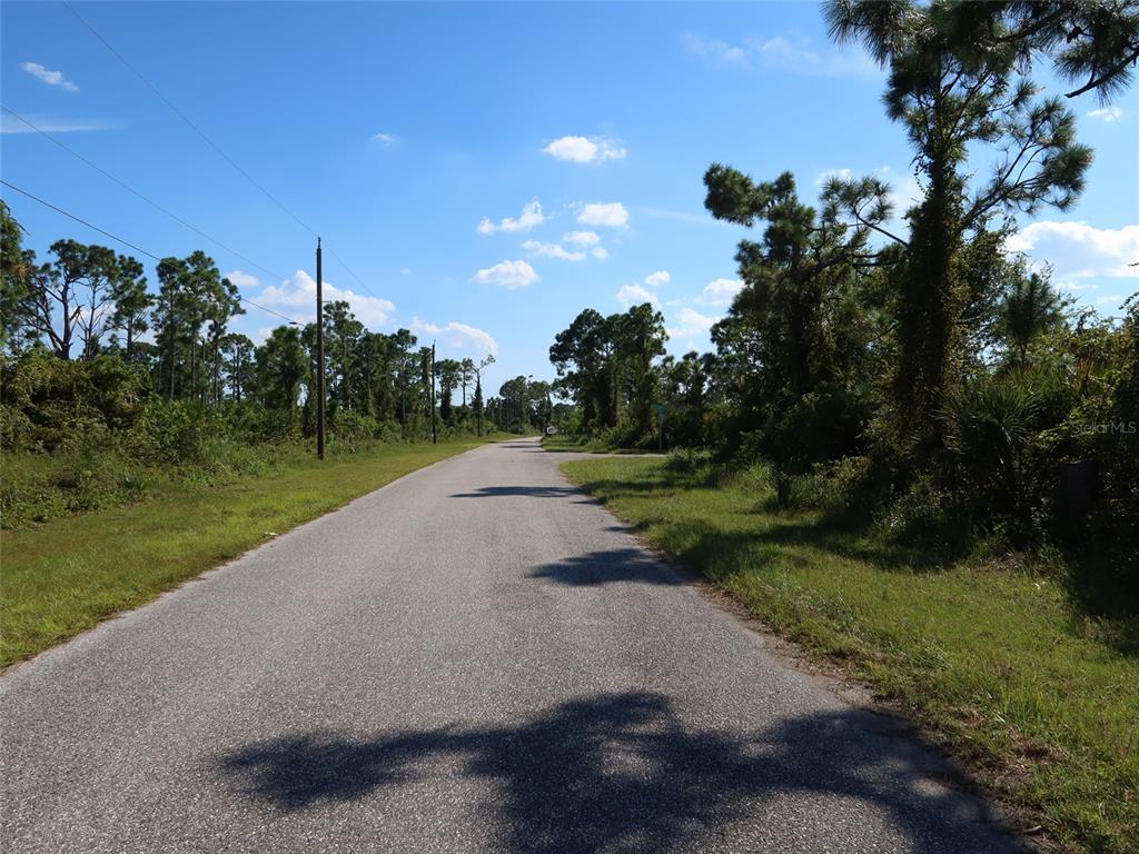 A paved road stretches through a rural, wooded area under a blue sky — 8185 DIMSTEAD STREET, PORT CHARLOTTE, FL