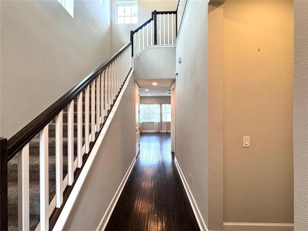 A hallway with dark wood flooring leads to a room with windows and a staircase — 13808 CHAUVIN AVENUE, ORLANDO, FL